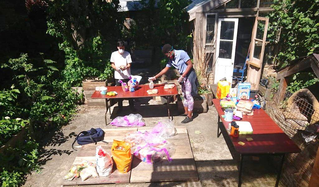 Two people in a backyard, in the sunshine. They are working on a project on a table.