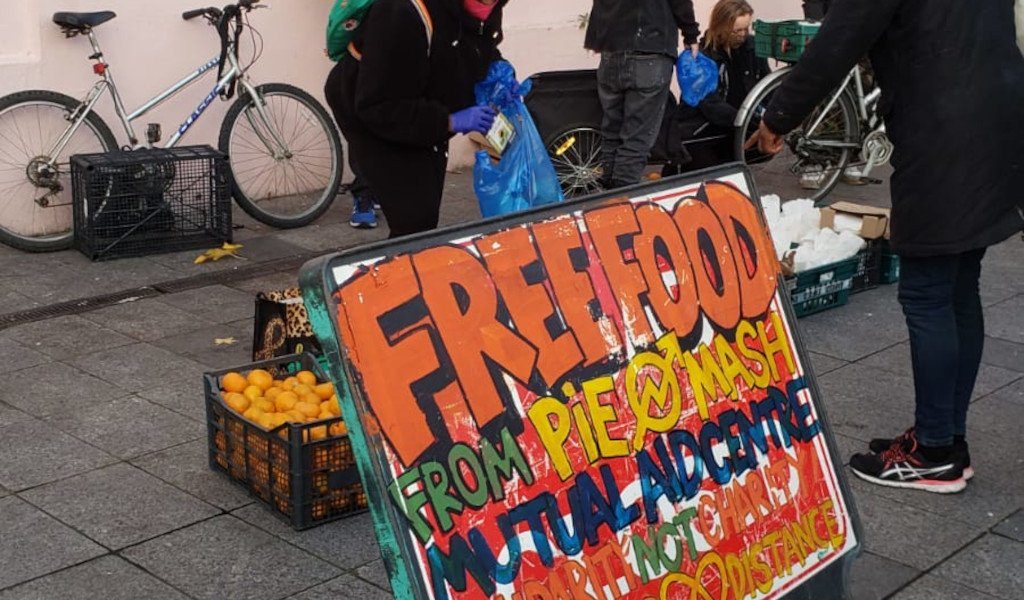 Weekly stall at Deptford library square, sign with "free food" and people bagging up food.